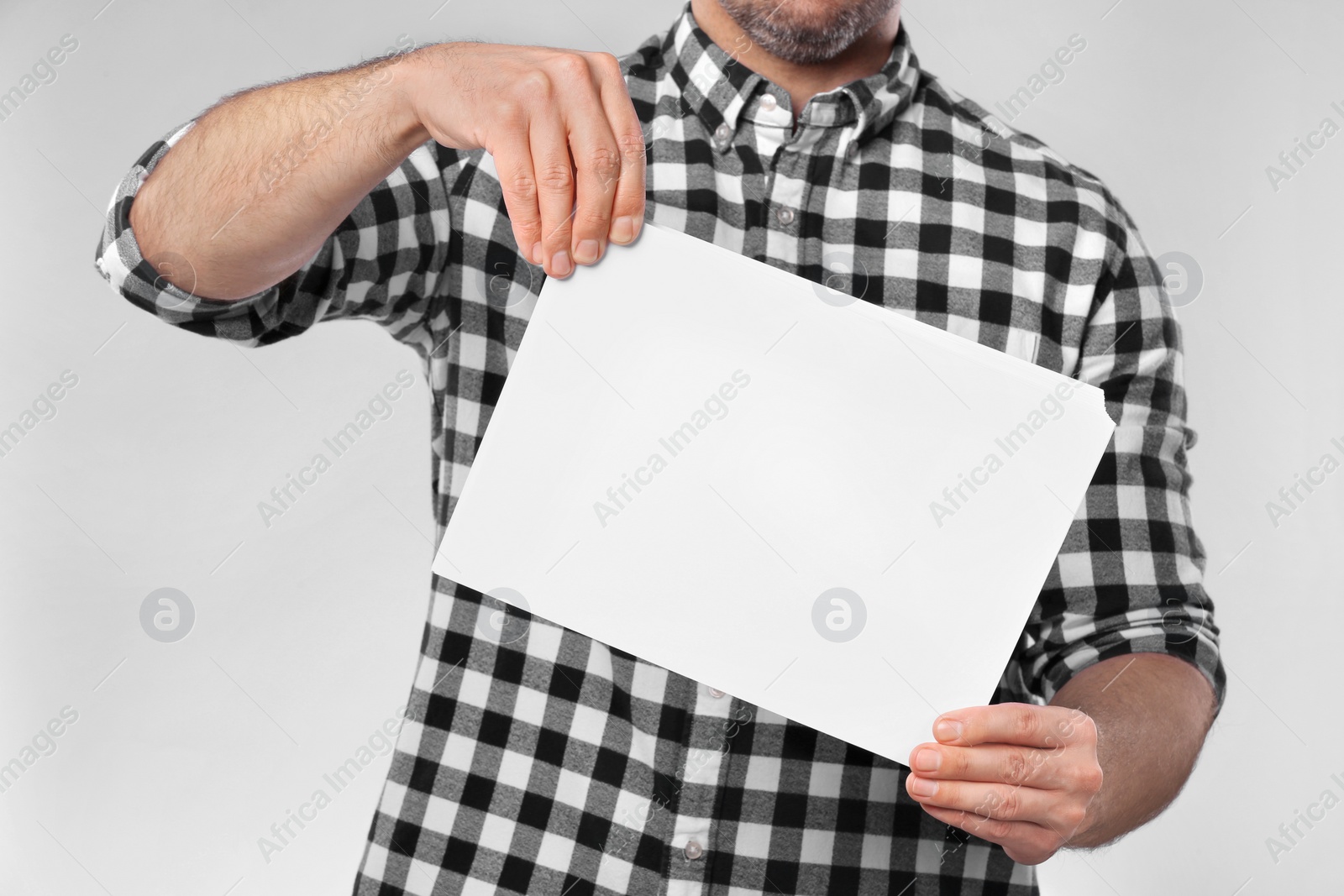 Photo of Man holding sheet of paper on light grey background, closeup. Mockup for design