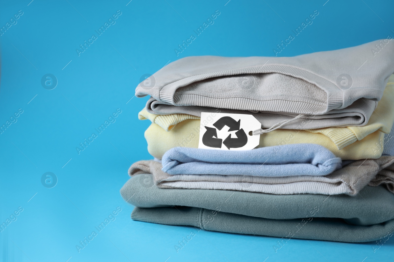 Photo of Clothes with recycling label on light blue background, space for text