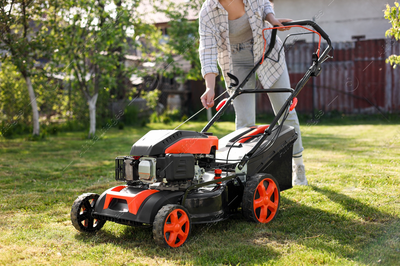 Photo of Woman cutting green grass with lawn mower in garden, closeup