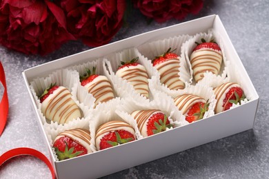 Photo of Delicious chocolate covered strawberries in box and flowers on light grey table