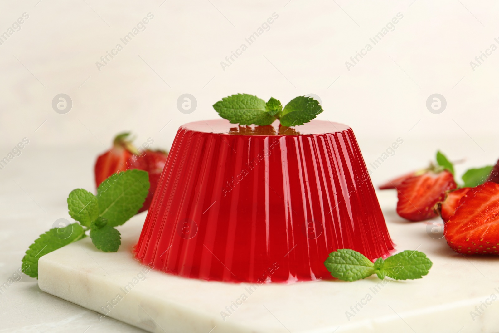 Photo of Stone board with fruit jelly, strawberries and mint on light table