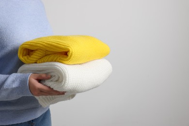 Photo of Woman with knitted sweaters on light background, closeup. Space for text