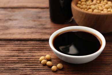 Soy sauce in bowl and soybeans on wooden table, closeup. Space for text