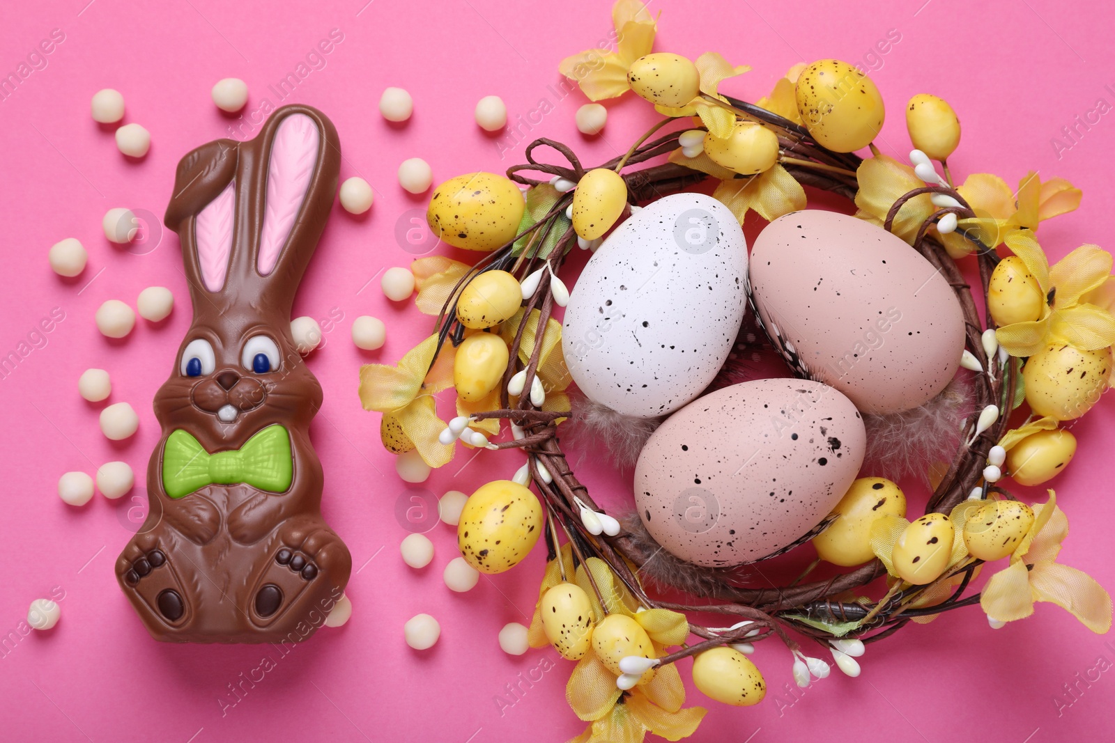 Photo of Flat lay composition with chocolate Easter bunny, festively decorated eggs and candies on pink background