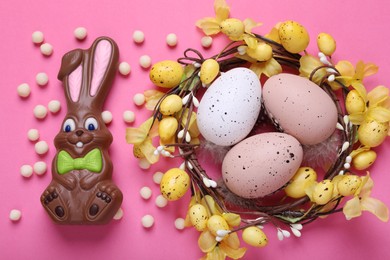 Photo of Flat lay composition with chocolate Easter bunny, festively decorated eggs and candies on pink background