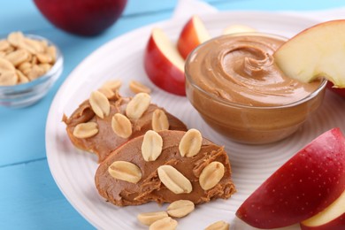 Photo of Slices of fresh apple with peanut butter and nuts on light blue wooden table, closeup