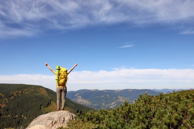 Photo of Young woman with backpack on rocky peak in mountains, back view