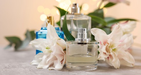 Photo of Bottles of perfume and beautiful lily flowers on table against beige background with blurred lights, closeup