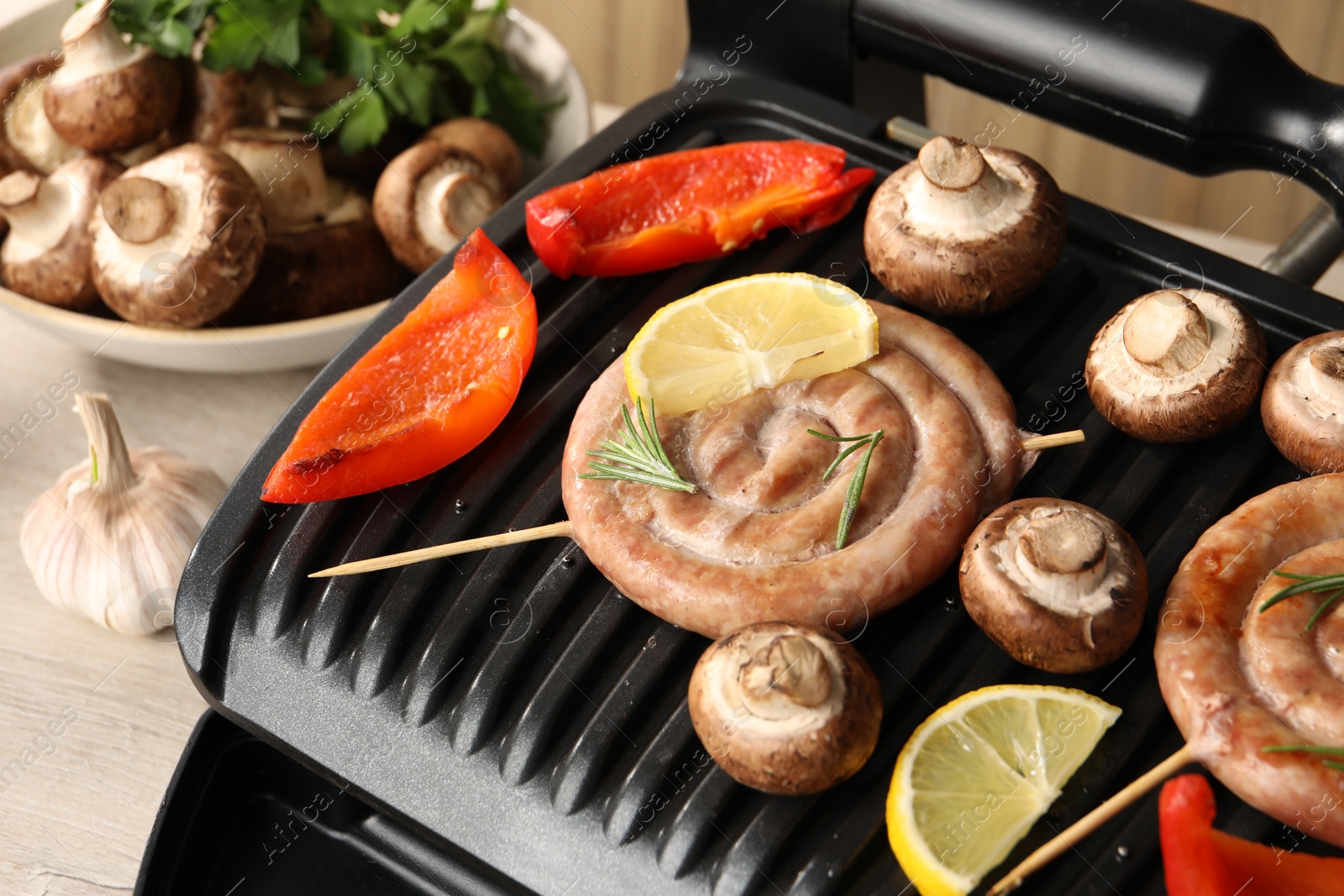 Photo of Electric grill with homemade sausages, mushrooms and bell pepper on table, closeup