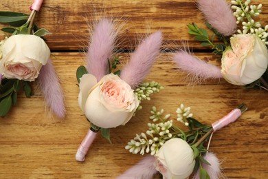 Many stylish boutonnieres on wooden table, flat lay