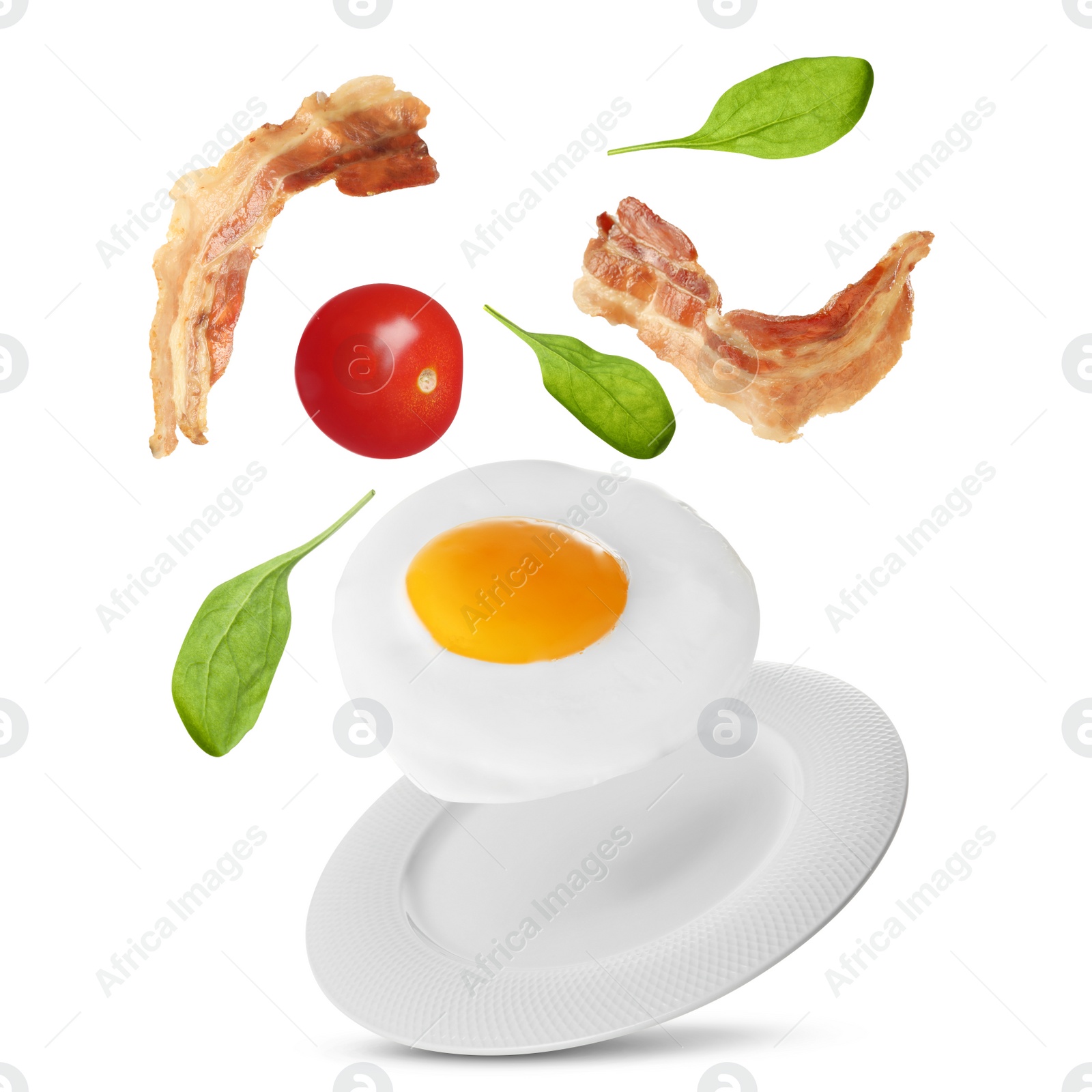 Image of Tasty fried chicken egg, bacon, tomato and basil leaves falling into plate on white background