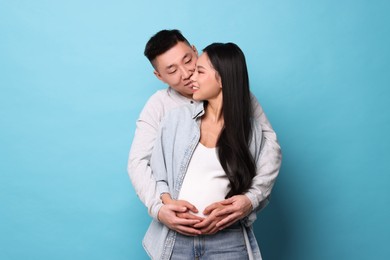 Photo of Man touching his pregnant wife's belly on light blue background