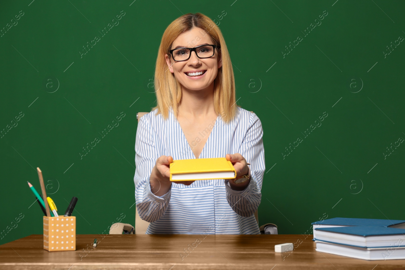 Photo of Portrait of beautiful teacher sitting at table near chalkboard