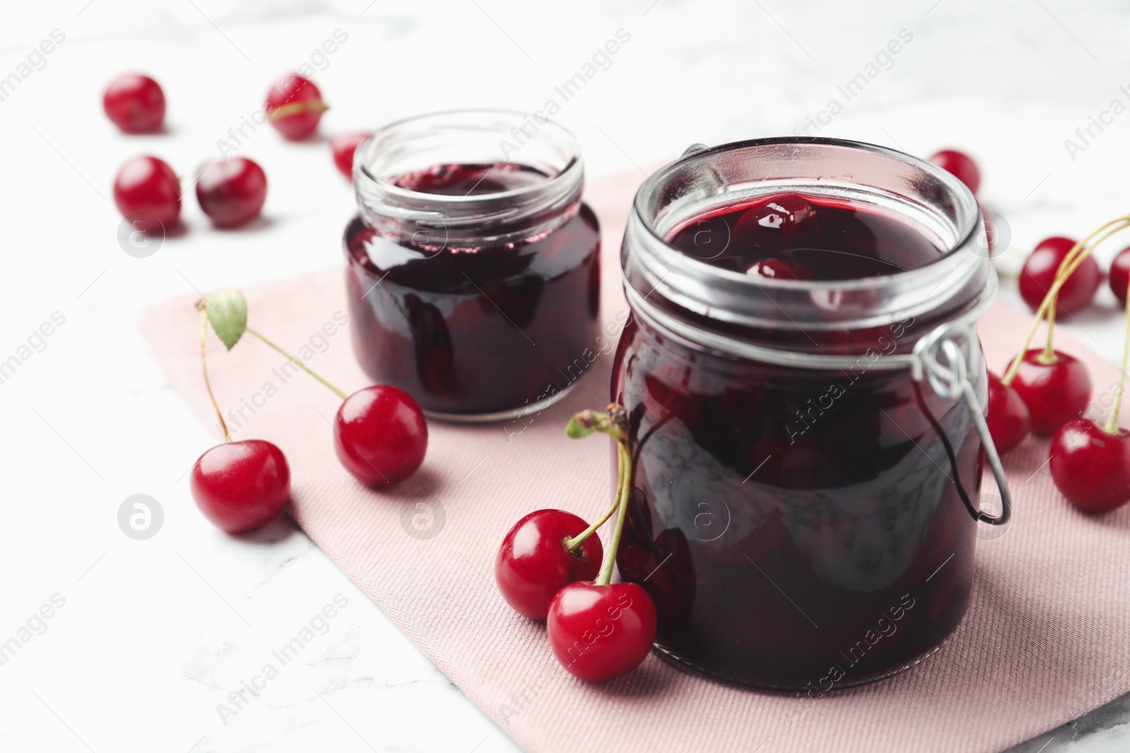 Photo of Jars of pickled cherries and fresh fruits on table, closeup