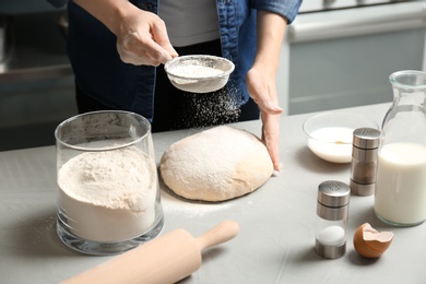 Woman sprinkling flour over dough on table in kitchen