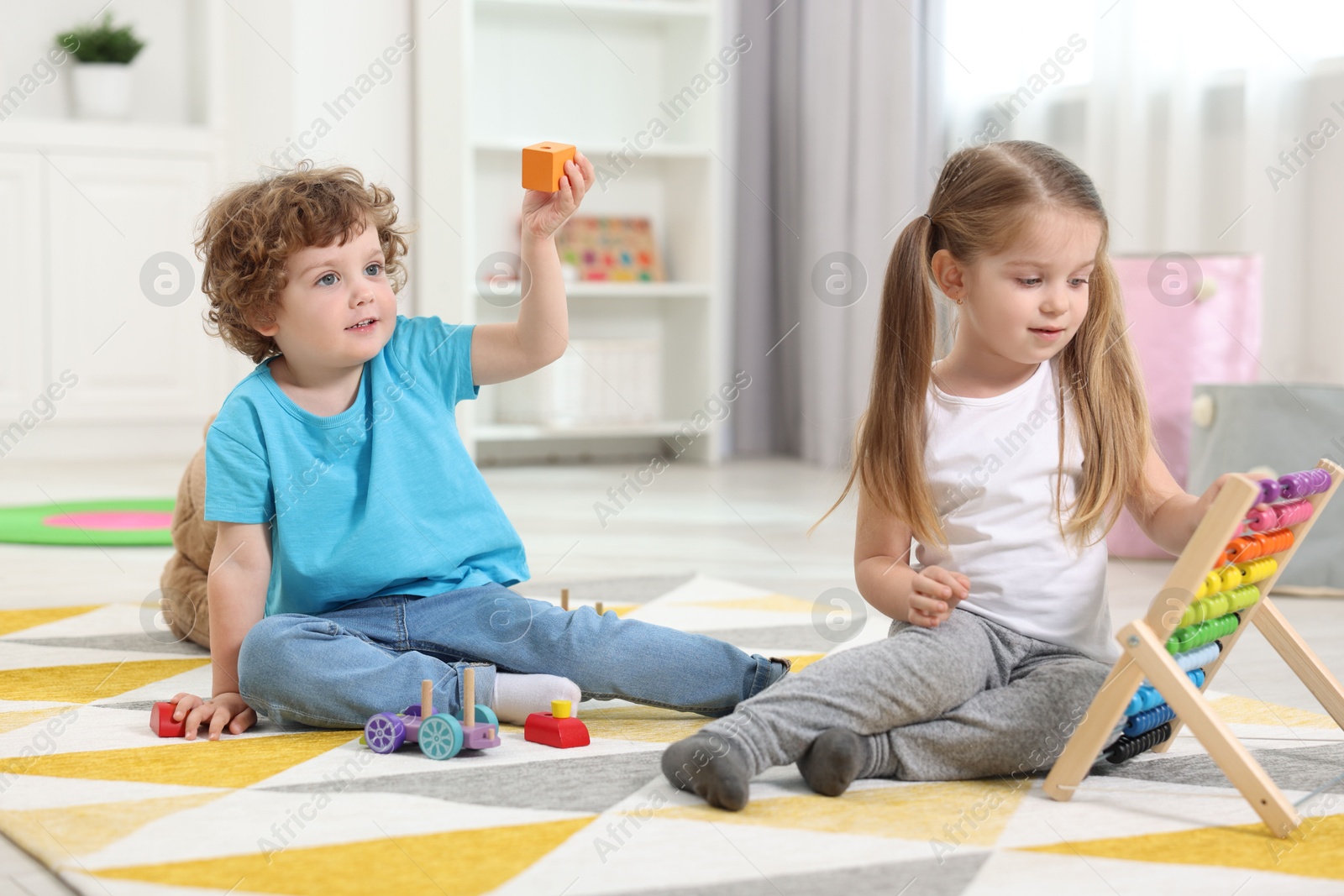 Photo of Cute little children playing with different toys on floor in kindergarten