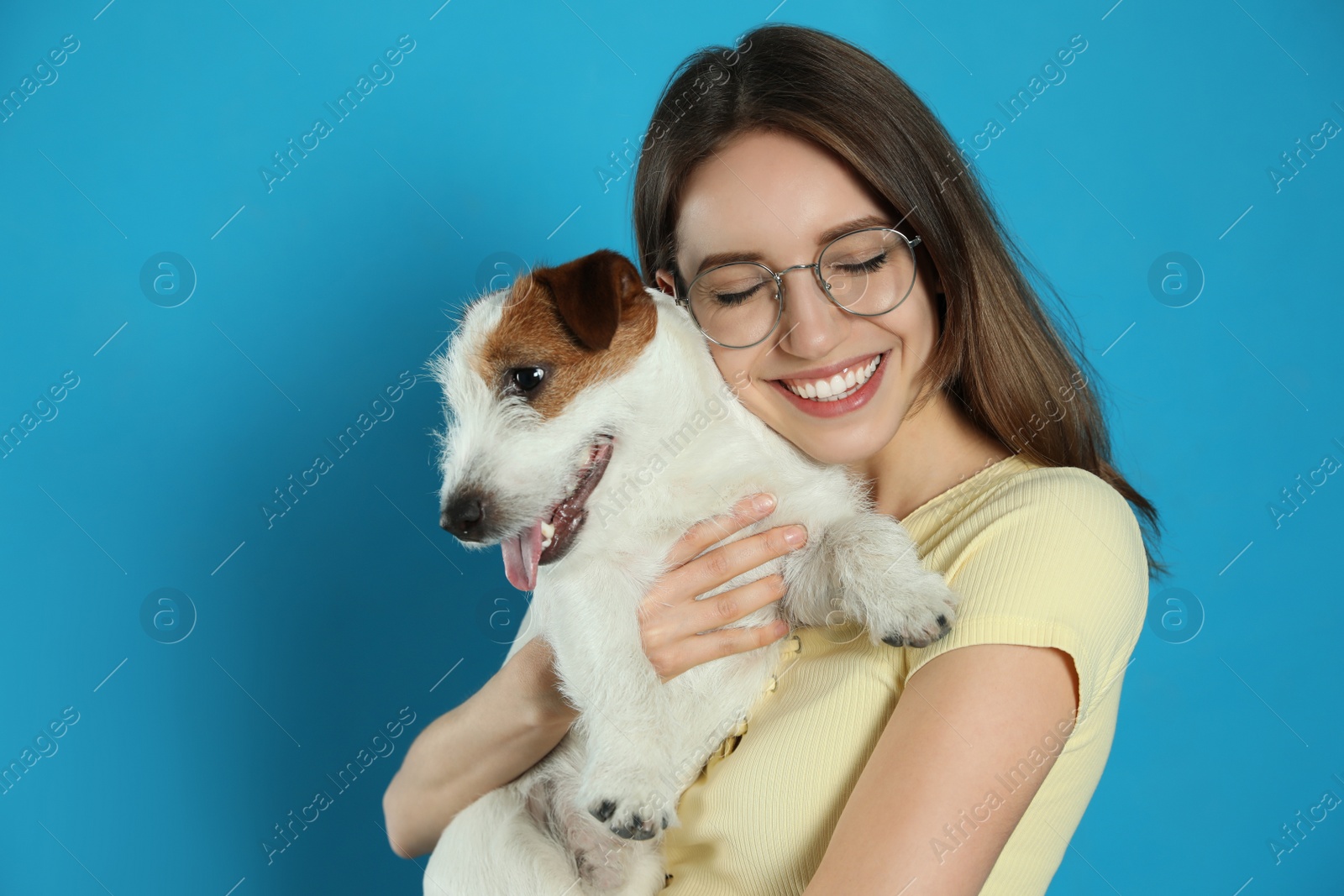 Photo of Young woman with her cute Jack Russell Terrier on light blue background. Lovely pet