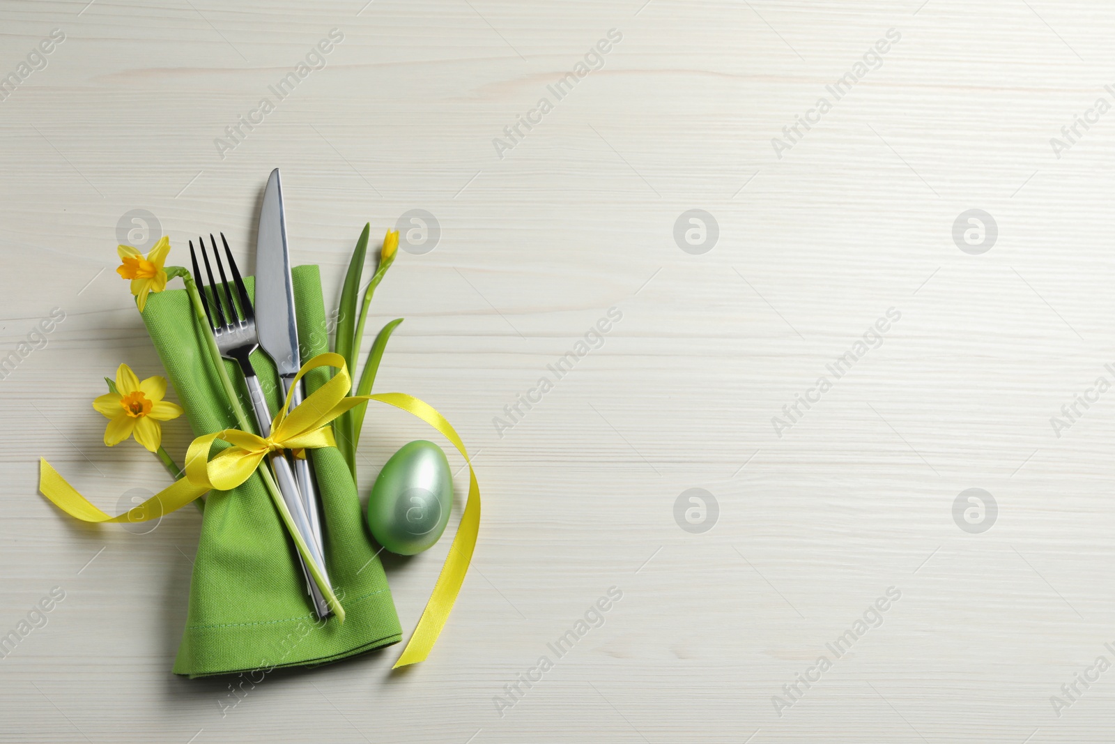 Photo of Cutlery set, painted egg and beautiful flowers on wooden table, flat lay with space for text. Easter celebration