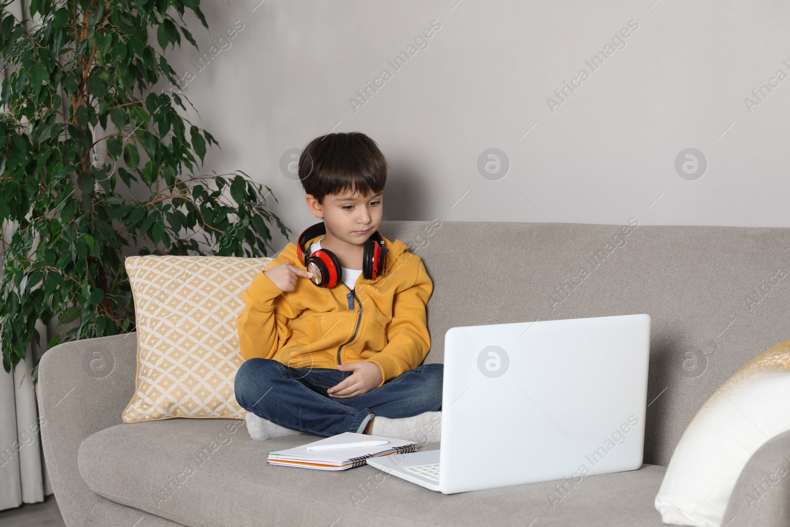 Photo of Cute little boy with modern laptop studying online at home. E-learning