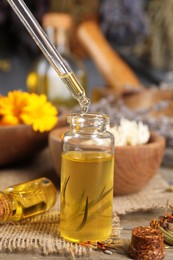 Dripping herbal essential oil from pipette into bottle on wooden table