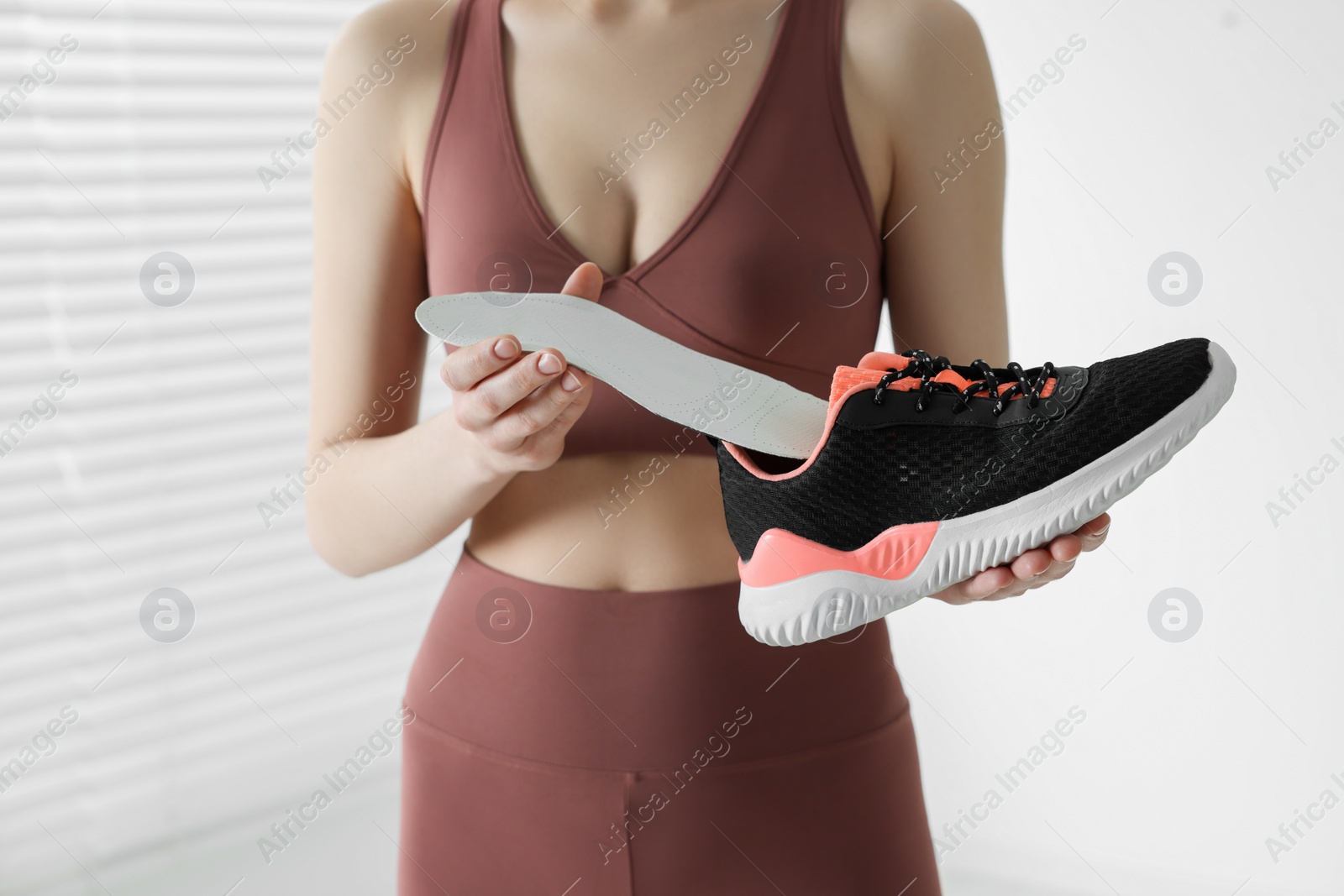 Photo of Sporty woman putting orthopedic insole into shoe indoors, closeup. Foot care