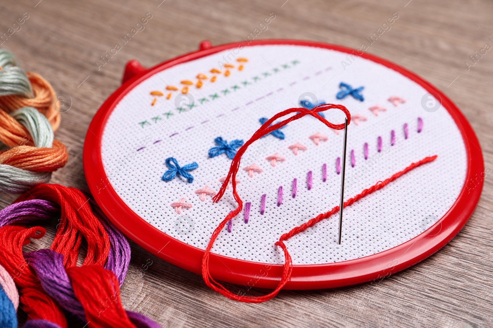Photo of Embroidery hoop with fabric, needle and colorful floss set on wooden table, closeup