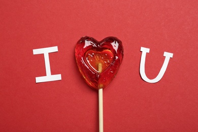 Photo of Phrase I Love You made of paper letters and heart shaped lollipop on red background, flat lay