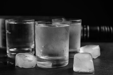 Photo of Vodka in shot glasses with ice on table against black background, closeup