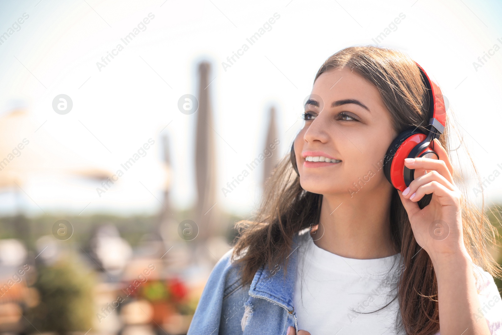 Photo of Young woman with headphones listening to music outdoors. Space for text