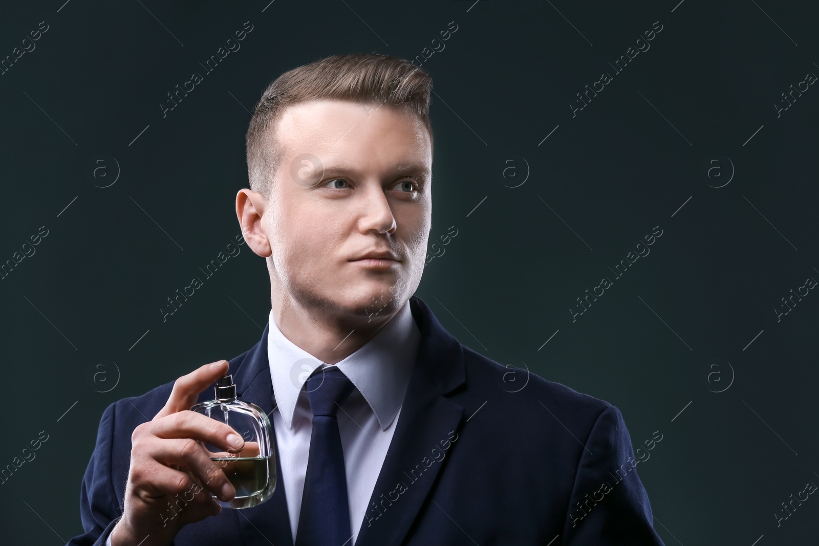 Photo of Handsome man in suit using perfume on dark background