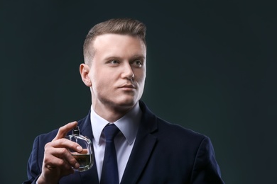 Photo of Handsome man in suit using perfume on dark background