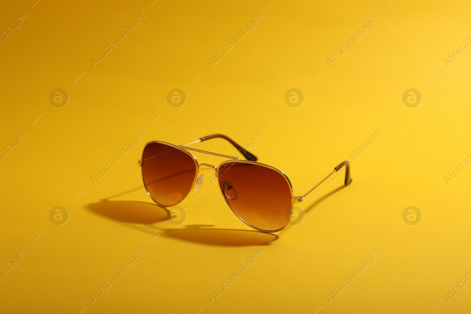 Photo of Stylish pair of sunglasses on yellow background