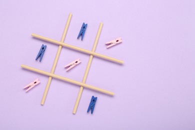 Photo of Tic tac toe game made with clothespins on lilac background, top view