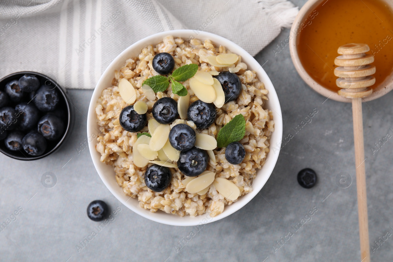 Photo of Tasty oatmeal with blueberries, mint and almond petals in bowl on grey table, flat lay