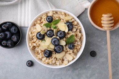 Photo of Tasty oatmeal with blueberries, mint and almond petals in bowl on grey table, flat lay