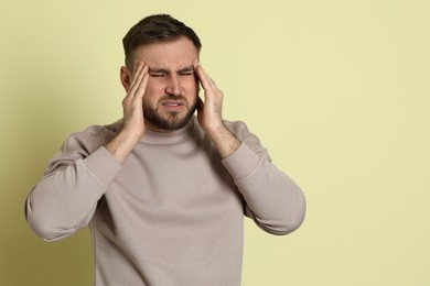 Photo of Man suffering from migraine on light green background. Space for text