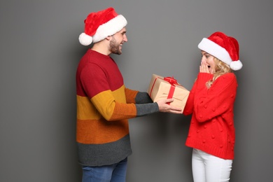 Photo of Young couple in Santa hats with Christmas gift on grey background