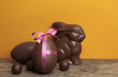 Photo of Composition with chocolate Easter eggs and bunny on table against color background. Space for text