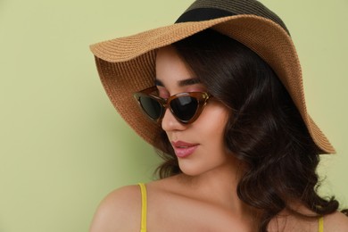 Beautiful young woman with straw hat and stylish sunglasses on light green background