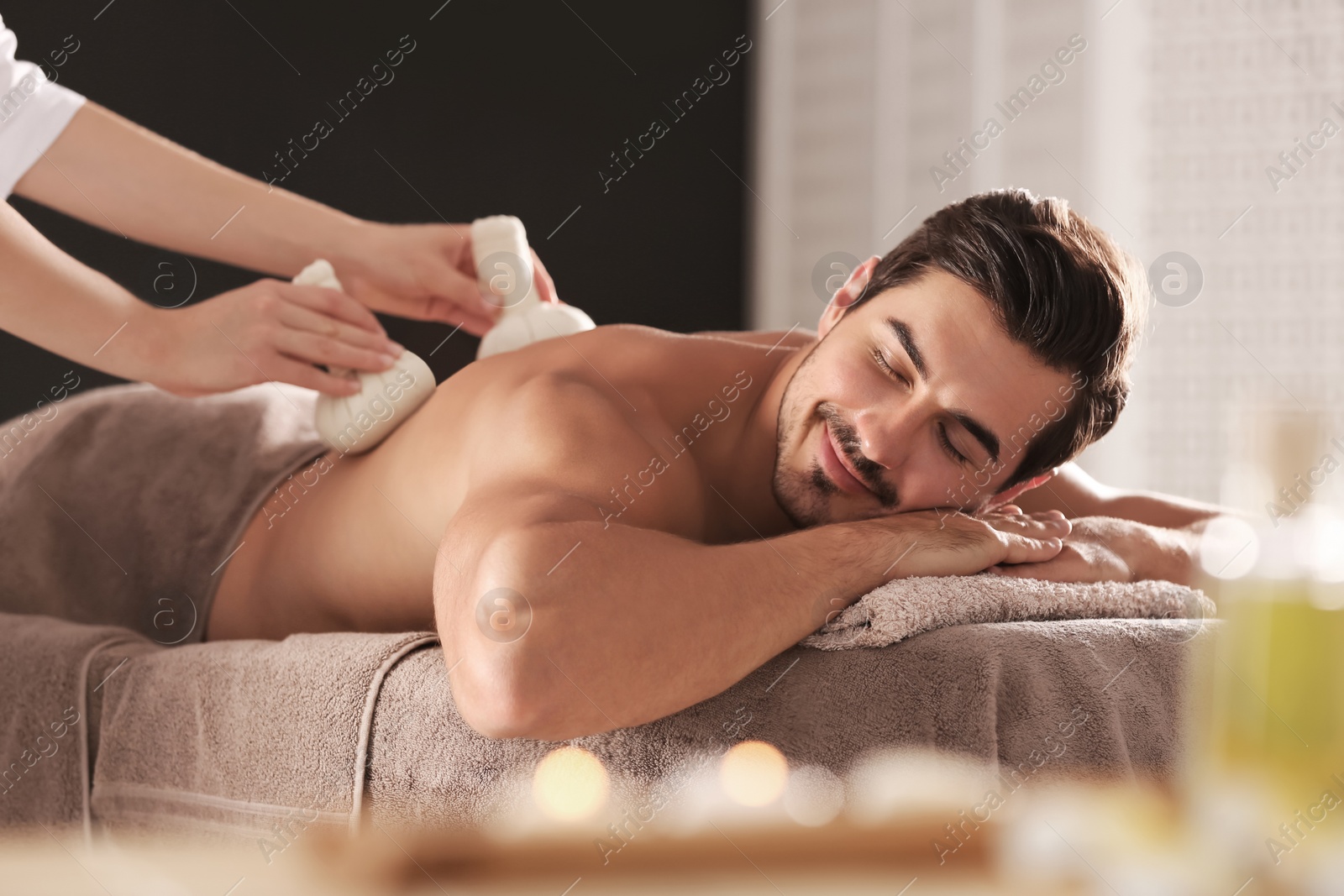 Photo of Handsome young man receiving herbal bag massage in spa salon