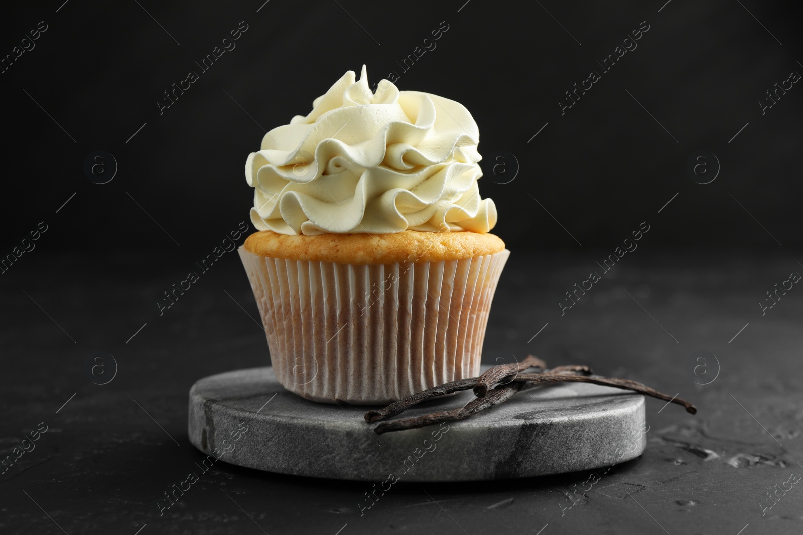 Photo of Tasty cupcake with cream and vanilla pods on black table, closeup