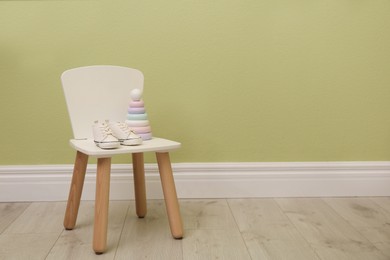 Chair with baby shoes and toy near green wall, space for text. Interior design