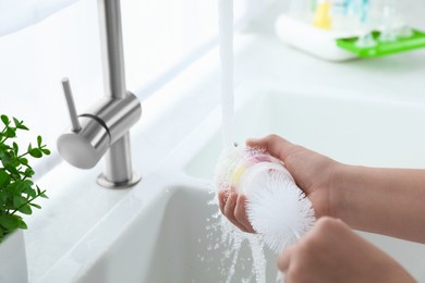 Photo of Woman washing baby bottle under stream of water in kitchen, closeup