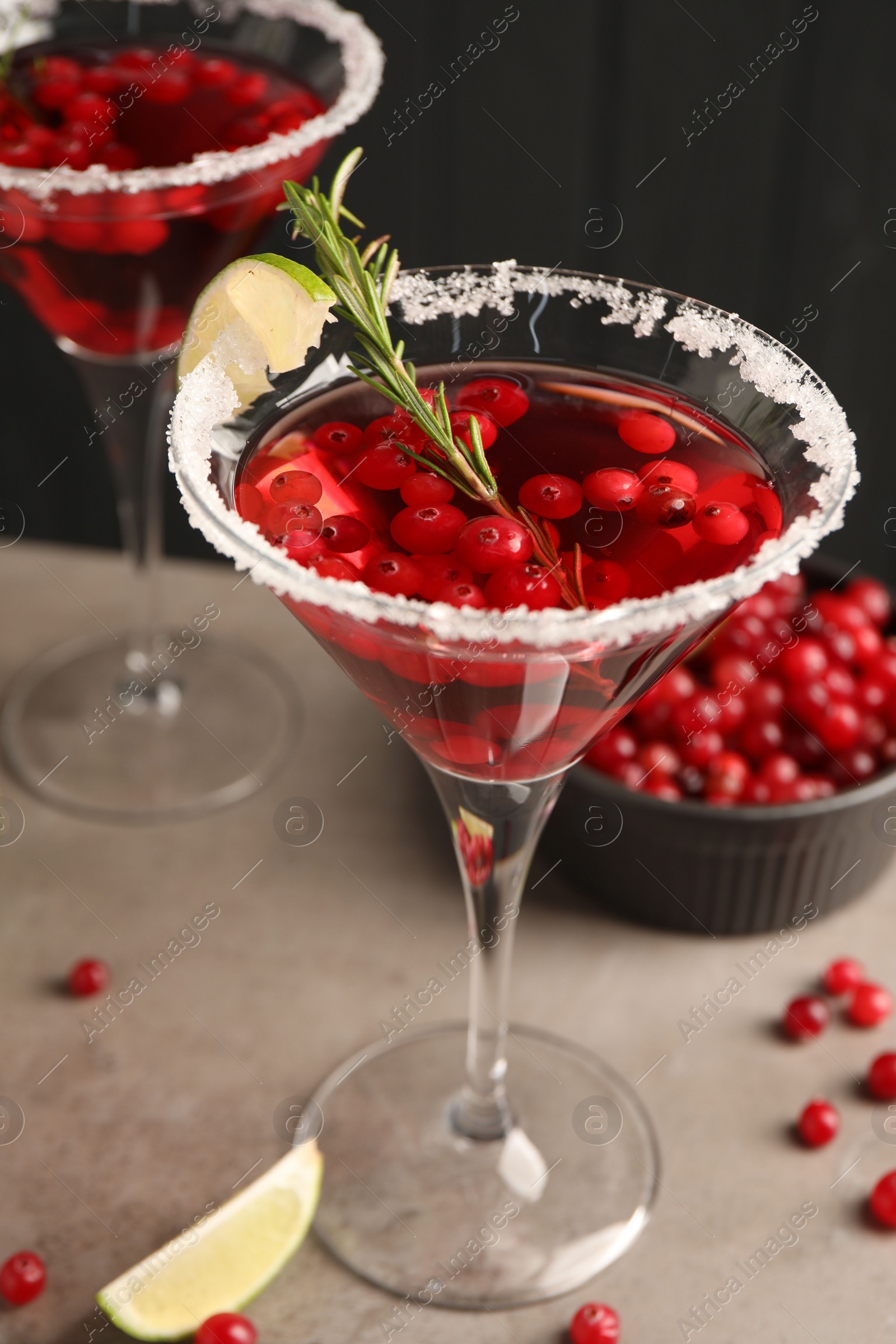 Photo of Tasty cranberry cocktail with rosemary and lime in glasses on grey table against black background, closeup