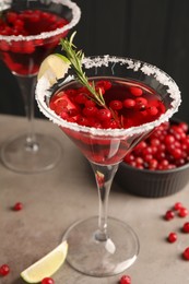 Tasty cranberry cocktail with rosemary and lime in glasses on grey table against black background, closeup