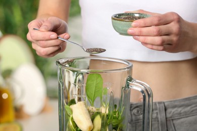 Woman adding chia seeds into blender with ingredients for green smoothie, closeup