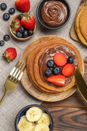 Photo of Tasty pancakes with chocolate paste, berries and banana served on wooden table, flat lay