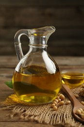 Glass jug with oil and soybeans on wooden table