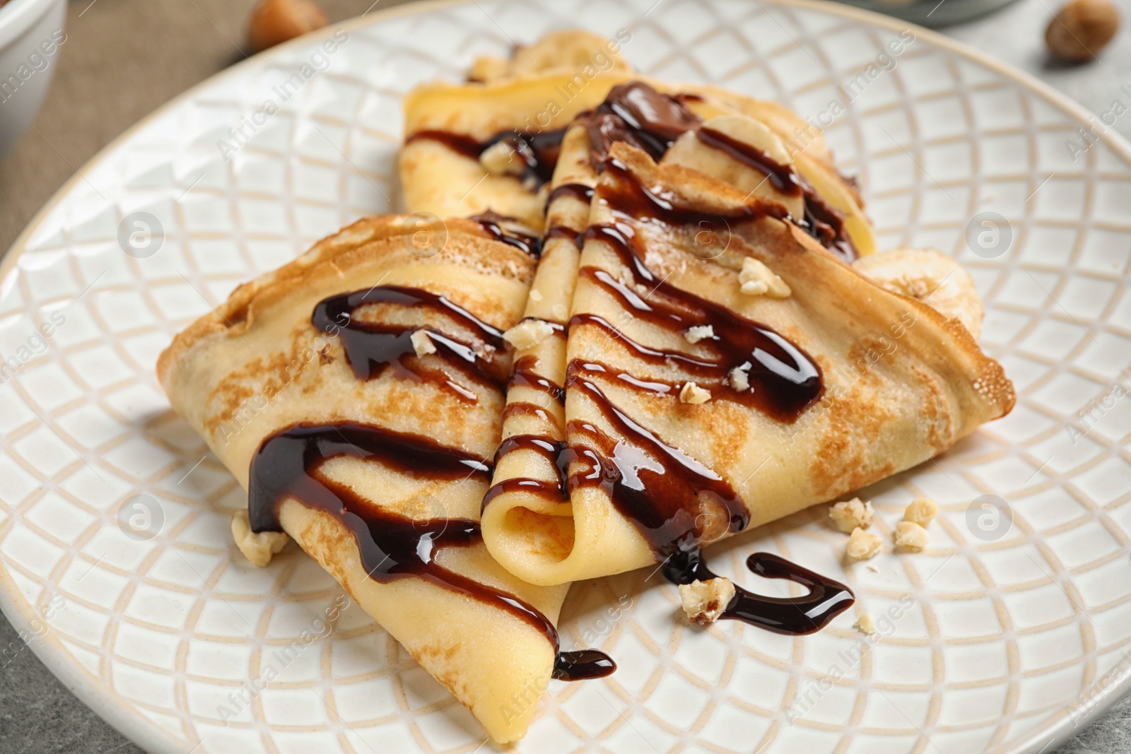 Photo of Delicious thin pancakes with chocolate spread, banana and nuts on plate, closeup