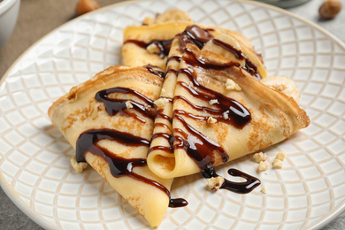 Delicious thin pancakes with chocolate spread, banana and nuts on plate, closeup